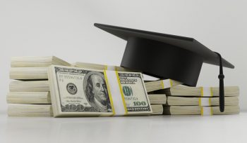 Several wads of hundred dollar bills with a graduation cap resting on top