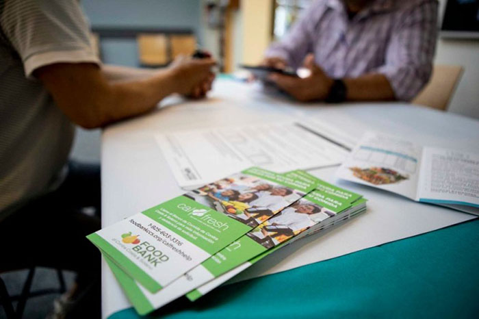 Food bank pamphlets on a table with other papers and 2 people sitting in the background