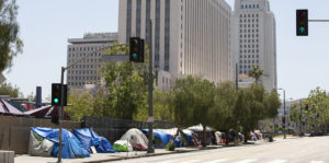 A street in Los Angeles, with a number of tents on the sidewalk and skyscrapers in the background