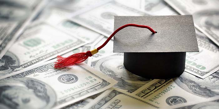 Graduation mortar cap sitting on top of scattered $100 bills