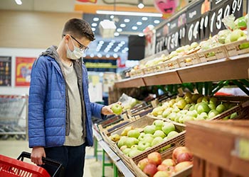 Teenager wearing protective mask picks fruits at grocery store.