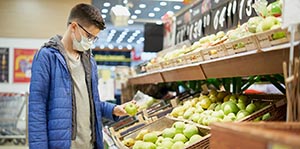 Teenager wearing protective mask picks fruits at grocery store.