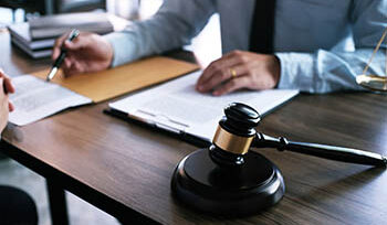 Two people sitting at a table, with a legal gavel, one person is explaining paperwork to another