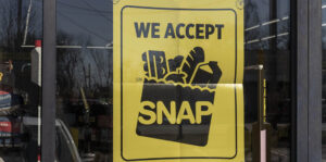A poster on a store window reads "WE ACCEPT EBT" with an icon of a shopping bag full of groceries