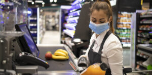 Cashier in supermarket wearing mask and gloves fully protected against corona virus. Working during covid-19 pandemic.