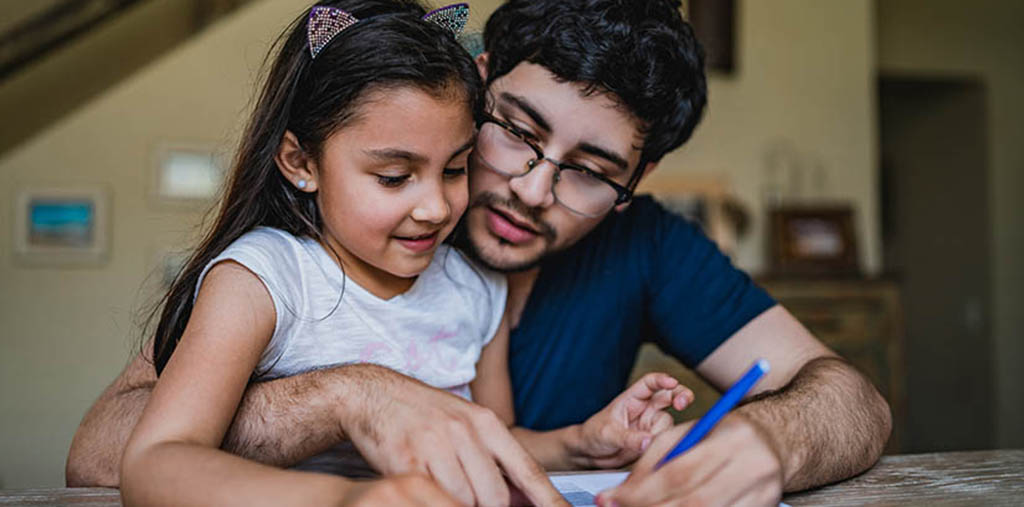 Image is a father with his daughter sitting on his lap. He has a pen and is signing something.